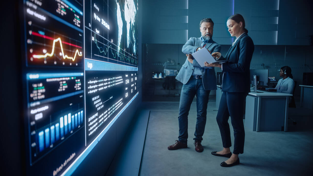 Two engineers reviewing network infrastructure dashboards on a large display in an operations centre.